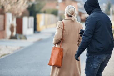Handbag mugging, woman facing away with coat and orange bag. Intimidating man in black reaching out towards her.